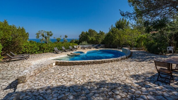 A stone pool with lounge chairs and a table, surrounded by greenery and a clear view of the sea. - Casa D'Aroeira - Serra d'Arrabida (Azeitão)