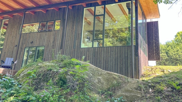 A modern wooden house with large windows and a covered porch.