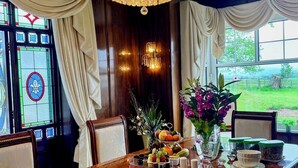 Une salle à manger avec une longue table en bois dressée pour le repas, un lustre et une vue sur l’extérieur.