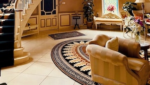Un grand escalier menant à l’étage supérieur, un lustre, une grande fenêtre avec des rideaux bleus et un arrangement floral sur une table.