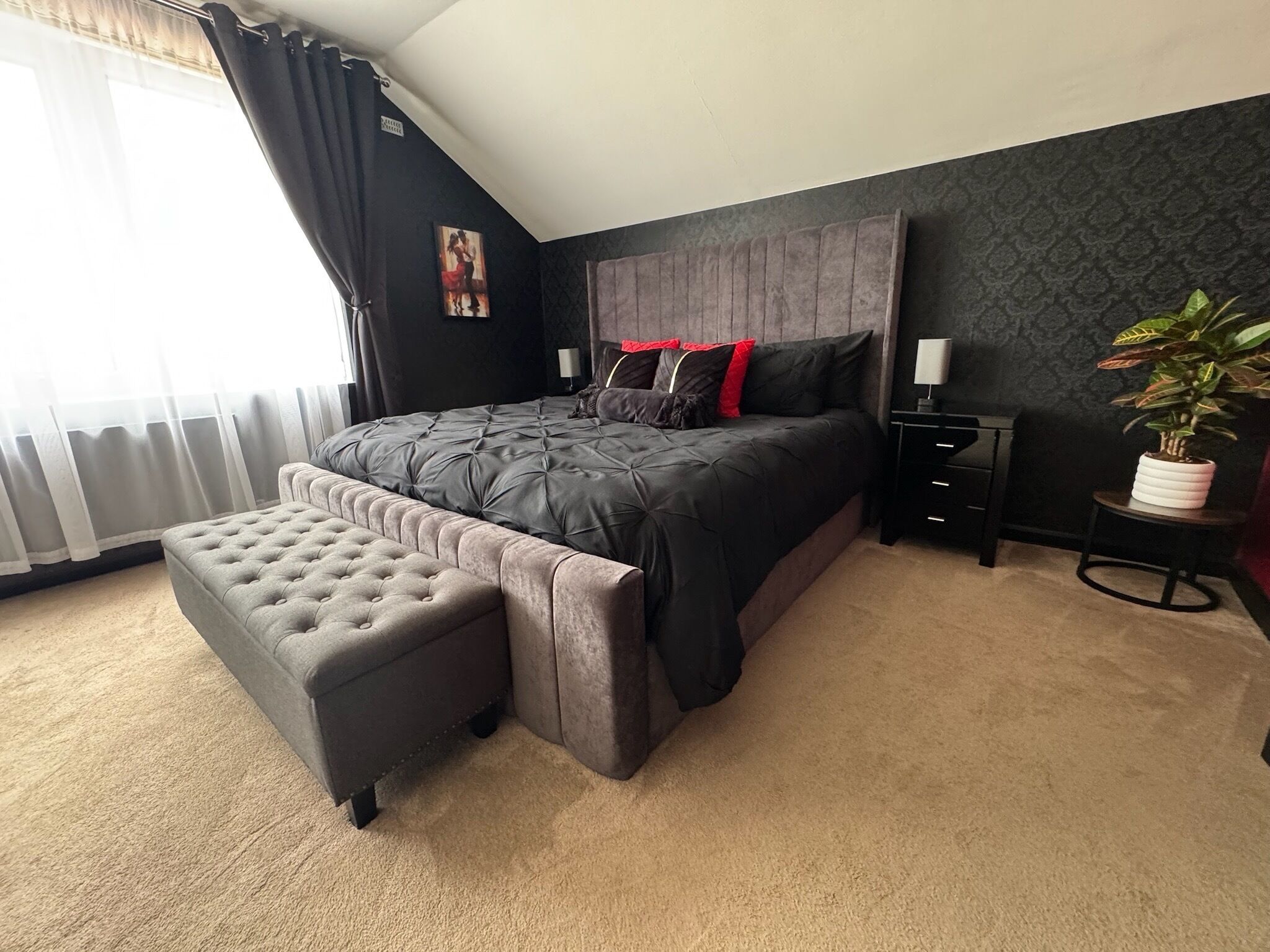 Ein Schlafzimmer mit einem großen Bett, einer Bank, einem Nachttisch, einer Lampe und einem Blumentopf.