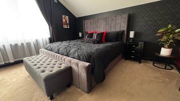 Ein Schlafzimmer mit einem großen Bett, einer Bank, einem Nachttisch, einer Lampe und einem Blumentopf.
