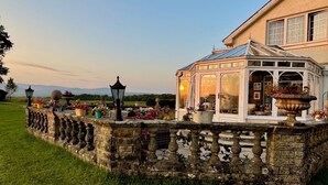 Une véranda dotée d’une balustrade en pierre, de plantes en pot et offrant une vue sur la campagne.