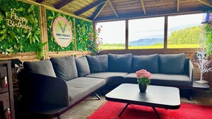 A cozy room with a grey sectional sofa, a small table with a pink flower vase, and a red rug. There's a 'Happy Birthday' sign and a 'Finn Village' sign on the wall. - FINN VILLAGE Raspberry Cottage HOT TUB Gazebo Private Garden (Glasgow)