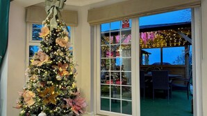A well-lit indoor space with a large Christmas tree decorated with lights and ornaments. - FINN VILLAGE Raspberry Cottage HOT TUB Gazebo Private Garden (Glasgow)