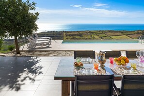 Een eethoek met een tafel voor vier personen, met uitzicht op een zwembad en de zee.