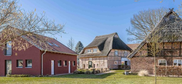 A traditional European village with red brick houses, a thatched-roof building, and a well-maintained lawn.
