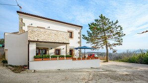Una casa a due piani con facciata in pietra, un balcone con piante in vaso e un'auto rossa parcheggiata nel vialetto.