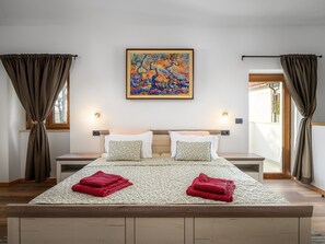 A bedroom with a bed, two bedside tables, a painting, and curtains.