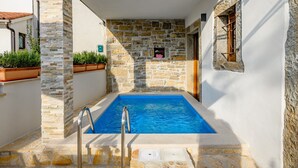 Una piscina con pareti in pietra e una scaletta metallica, circondata da un vialetto stretto.