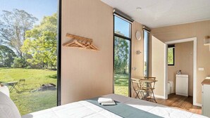 Une chambre avec une grande fenêtre, un lit, une petite table et une vue sur un espace verdoyant.