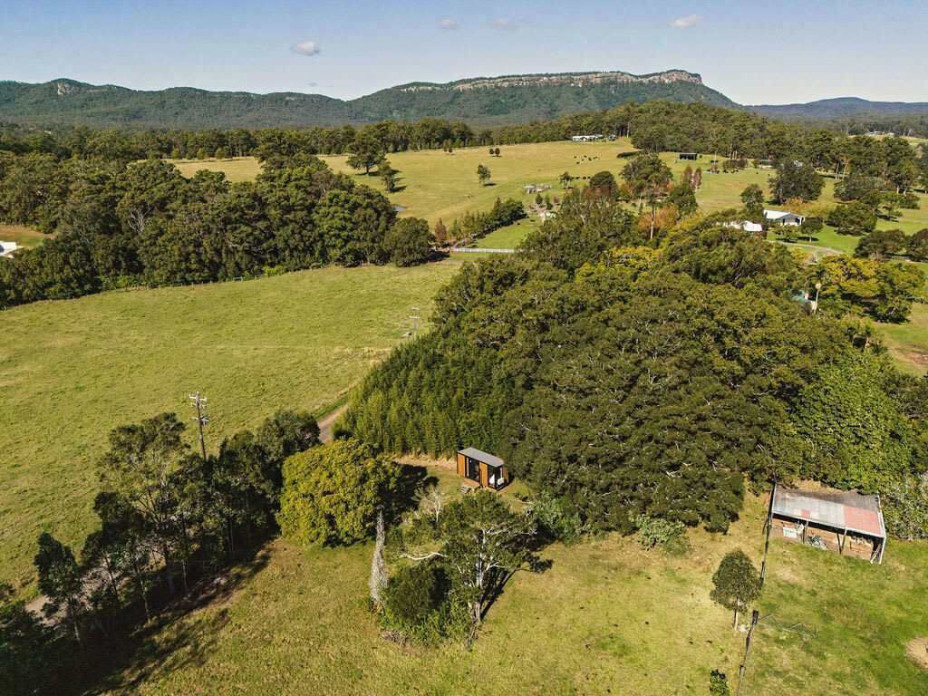 Vista aérea de un paisaje rural con una cabaña pequeña rodeada de árboles frondosos y campos abiertos.