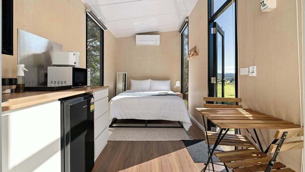 Une pièce compacte comprenant un lit, une petite kitchenette, une table à manger et de grandes fenêtres.