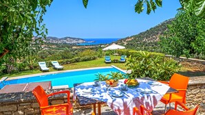 A poolside dining area with a table set for two, overlooking a pool and a scenic view of the sea and hills. - Bali private pool villa overlooking the lovely bay (Vlichada)