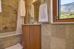 Ein Badezimmer mit einer Badewanne, einem Holzbadezimmer-Möbelstück und einem Fenster mit Blick auf eine gebirgige Landschaft.