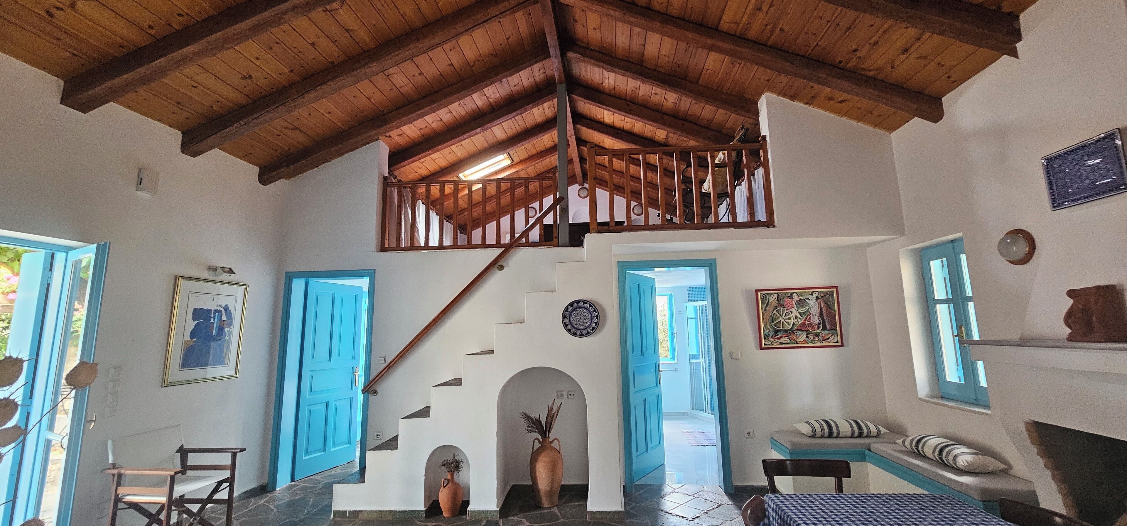 A spacious room with a high wooden ceiling, a staircase leading to an upper level, and a view of the outdoors through a large window.