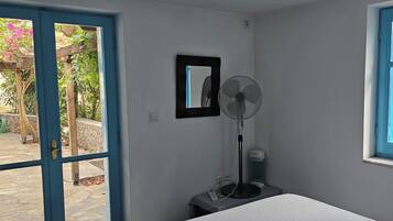 Una habitación con una cama, un ventilador, un espejo y una ventana con vistas a la vegetación.