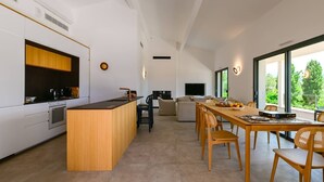 Une cuisine moderne dotée d’un îlot central, un coin repas avec une longue table et des chaises, et un espace de détente avec un canapé et un téléviseur.