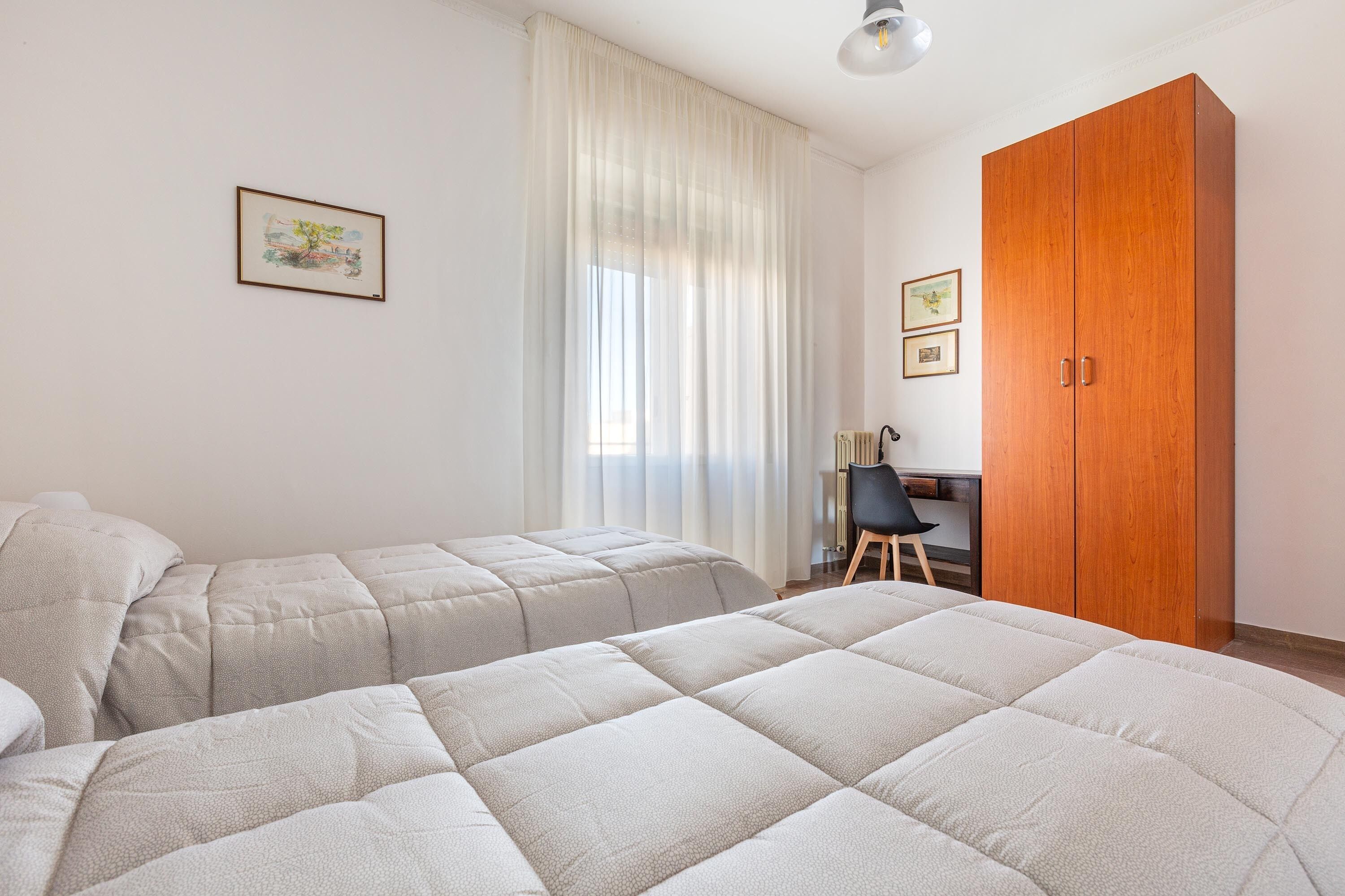 Ein Schlafzimmer mit zwei Betten, einem Holzschrank, einem Schreibtisch und zwei gerahmten Bildern an der Wand.