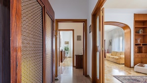 Um corredor com portas de madeira, parede estampada e uma sala de estar com sofá e mesa de centro.
