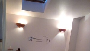 Un dormitorio con cama, mesita de noche, reloj de pared y luz en el techo.