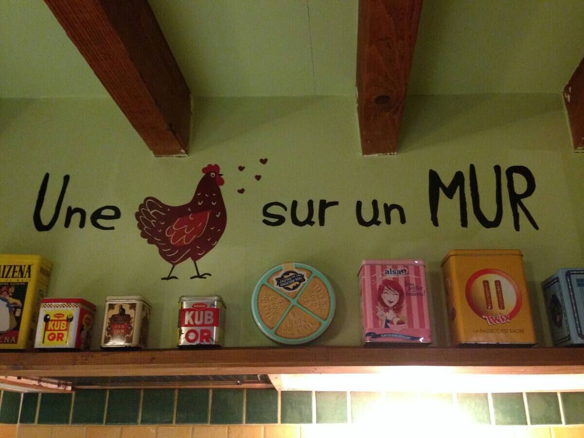 A wall with a chicken illustration and the text "Une sur un MUR" above a shelf with various food items.