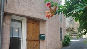 Un edificio con puerta de madera, una ventana y un buzón verde, todo a lo largo de una calle estrecha.