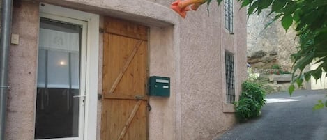 Un edificio con puerta de madera, una ventana y un buzón verde, todo a lo largo de una calle estrecha.