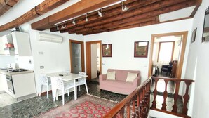A spacious living area with a kitchen, a dining table with chairs, a sofa, and a staircase with a wooden railing. - Ca' Rialto Apartment (Venezia)