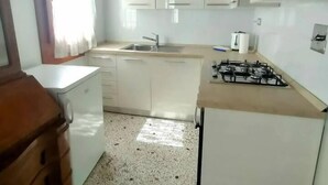 A kitchen with white cabinets, a gas stove, and a window with curtains. - Ca' Rialto Apartment (Venezia)