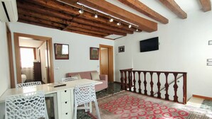 A room with a dining table, chairs, a sofa, a patterned rug, a wooden ceiling, and a staircase with a railing. - Ca' Rialto Apartment (Venezia)