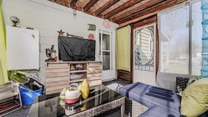 A compact living space with a kitchenette, a sofa, a glass-top coffee table, and a sliding glass door leading to a patio. - By The Beach - Affordable Sauble Beach Getaway (Sauble Beach)