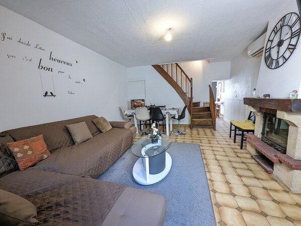 A cozy living room with a brown sofa, a glass coffee table, and a fireplace. A staircase leads to another room.