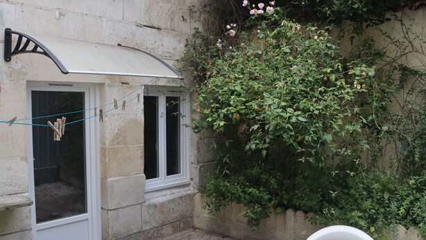 Un pequeño patio con mesa y sillas, un toldo blanco y una pared cubierta de plantas trepadoras y flores.