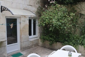 A small patio with a table and chairs, a white awning, and a wall covered with climbing plants and flowers.