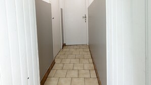 Un pasillo estrecho con paredes blancas y piso de baldosas, que lleva a una puerta cerrada.