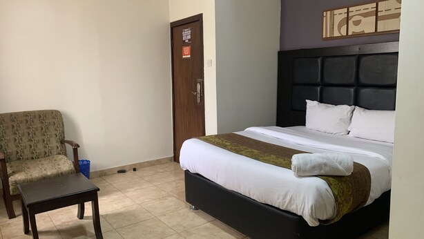 A hotel room with a bed, a chair, a small table, and a door with a sign. - FOSTER INN -ASAKE (Ibadan)