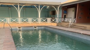 A swimming pool with a tiled edge, a covered area with white railings, and a building with a tiled facade in the background. - FOSTER INN -ASAKE (Ibadan)