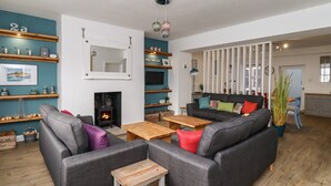 Ein gemütliches Wohnzimmer mit Kamin, grauen Sofas, einem Holztisch und Regalen mit diversen Gegenständen.