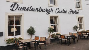 Fassade des Dunstanburgh Castle Hotels mit Schilder, Außenbereich mit Sitzgelegenheiten und Blumentöpfen.