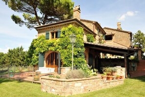 Una casa de piedra con una entrada abovedada grande, un porche cubierto y un jardín bien cuidado.