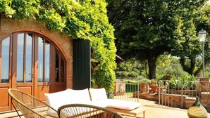 Un espace extérieur aménagé avec des chaises et une table en osier, une arche en briques et une vue sur la végétation environnante.