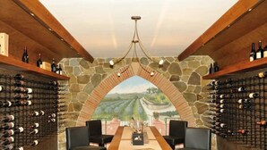Une cave à vin dotée d’une arche en pierre, de rangées de bouteilles de chaque côté et d’une table entourée de chaises au centre.