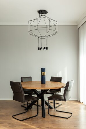 En matplats med ett runt träbord, svarta stolar, en modern, geometrisk taklampa och en blå vas med guldfärgade detaljer.