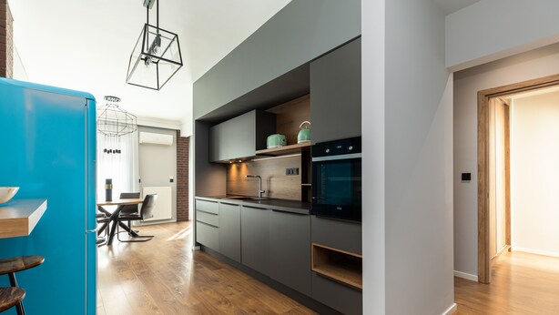 A modern kitchen with grey cabinetry, a blue refrigerator, and a dining area with a wooden table and chairs.