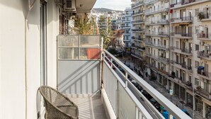 A balcony with two wicker chairs, a white railing, and a view of a cityscape with multi-story buildings.