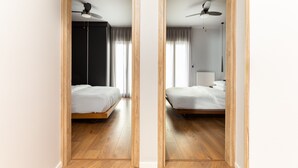 A mirrored view of a hotel room with a wooden floor, a bed, a ceiling fan, and a window with curtains.