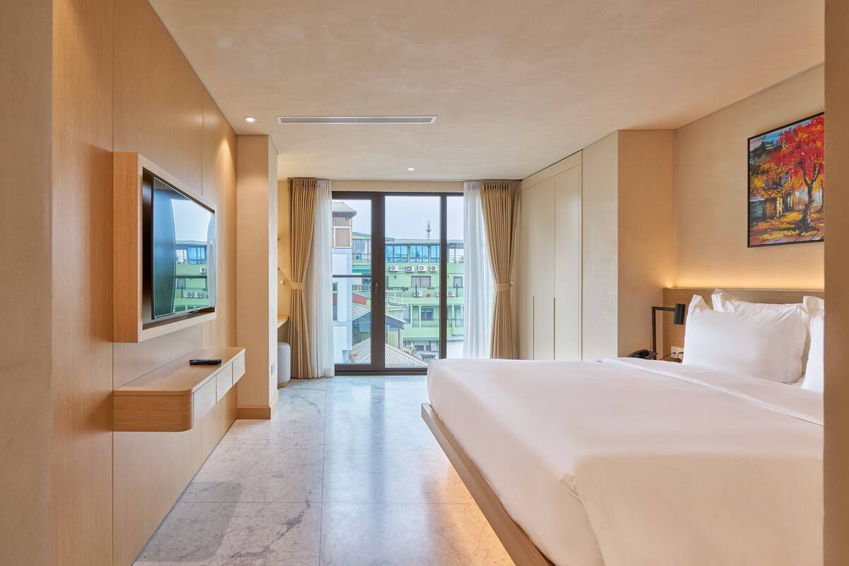 Habitación de hotel con una cama grande, un televisor montado en la pared, una puerta corrediza al balcón y un cuadro en la pared.