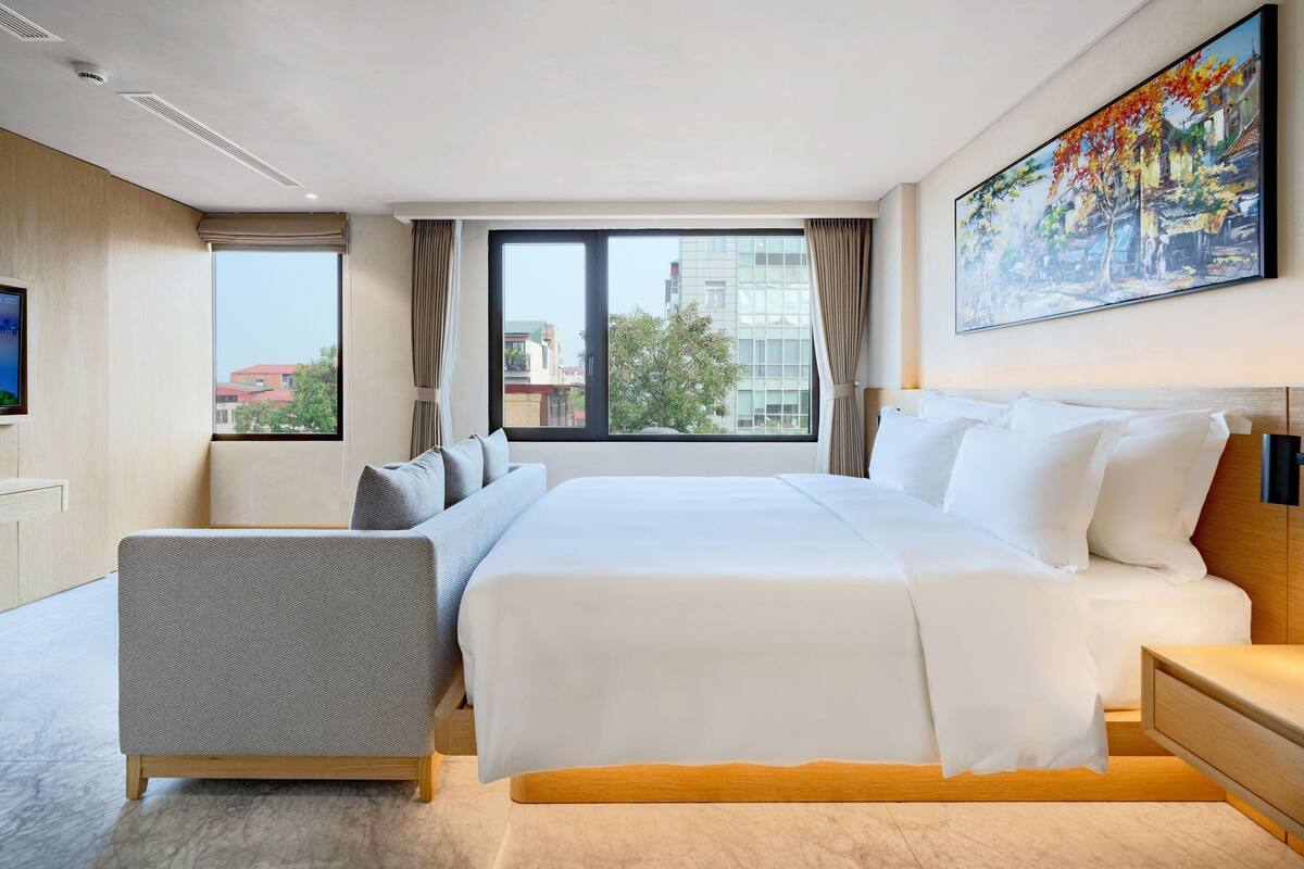 Habitación de hotel moderna con una cama grande, zona de estar, televisor y un cuadro en la pared.