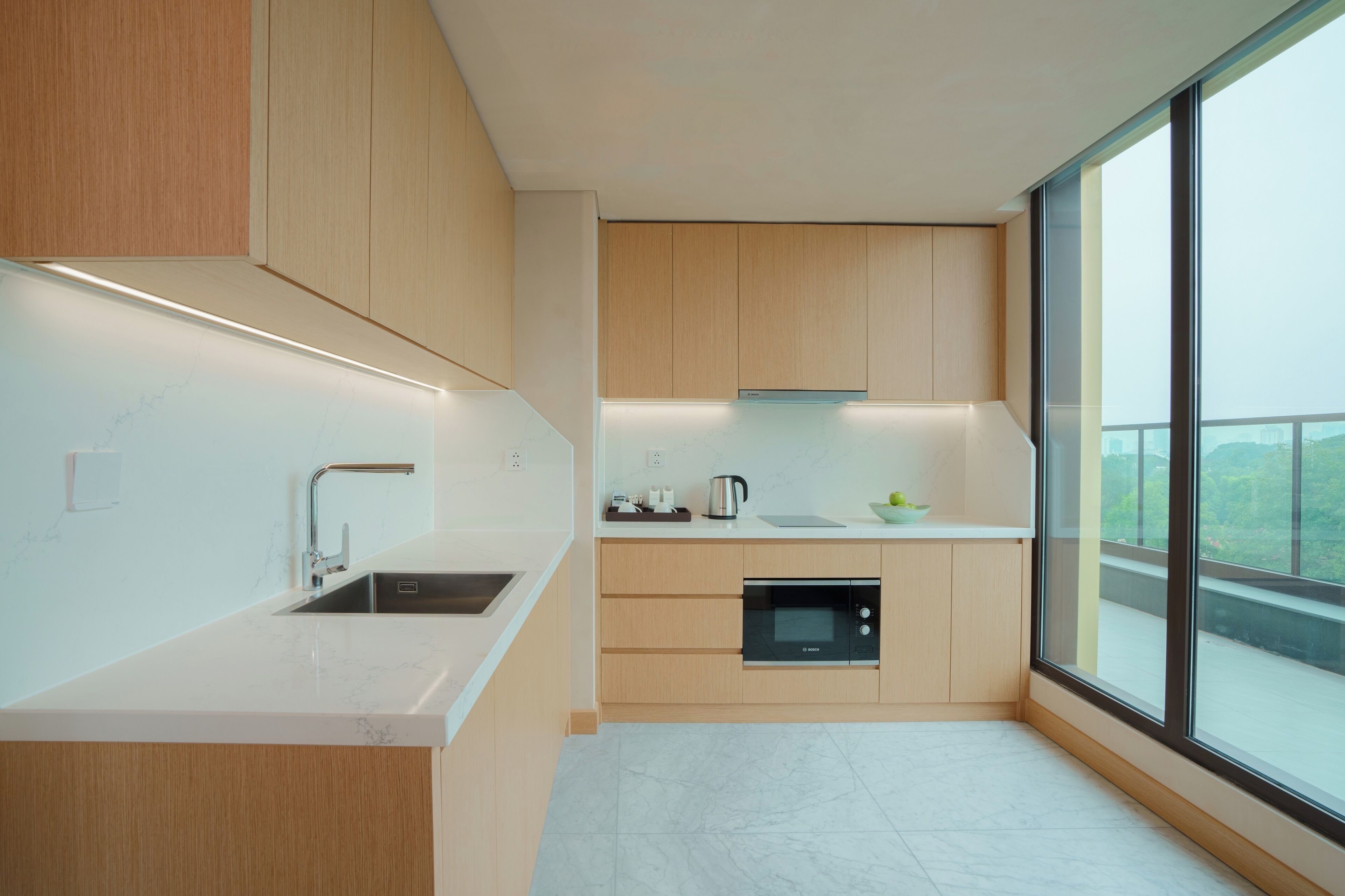 A modern kitchen with wooden cabinets, a built-in oven, and a large window offering a view.